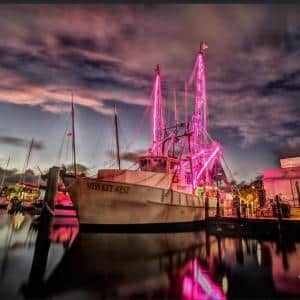 miss key west boat lit up in pink and purple lights at night time.
