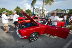 two people standing outside of a red car in a car show.
