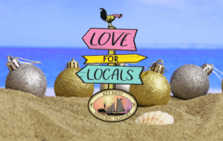 Christmas ornaments sitting on a beach with a Historic Seaport love for locals logo in the front of the picture.